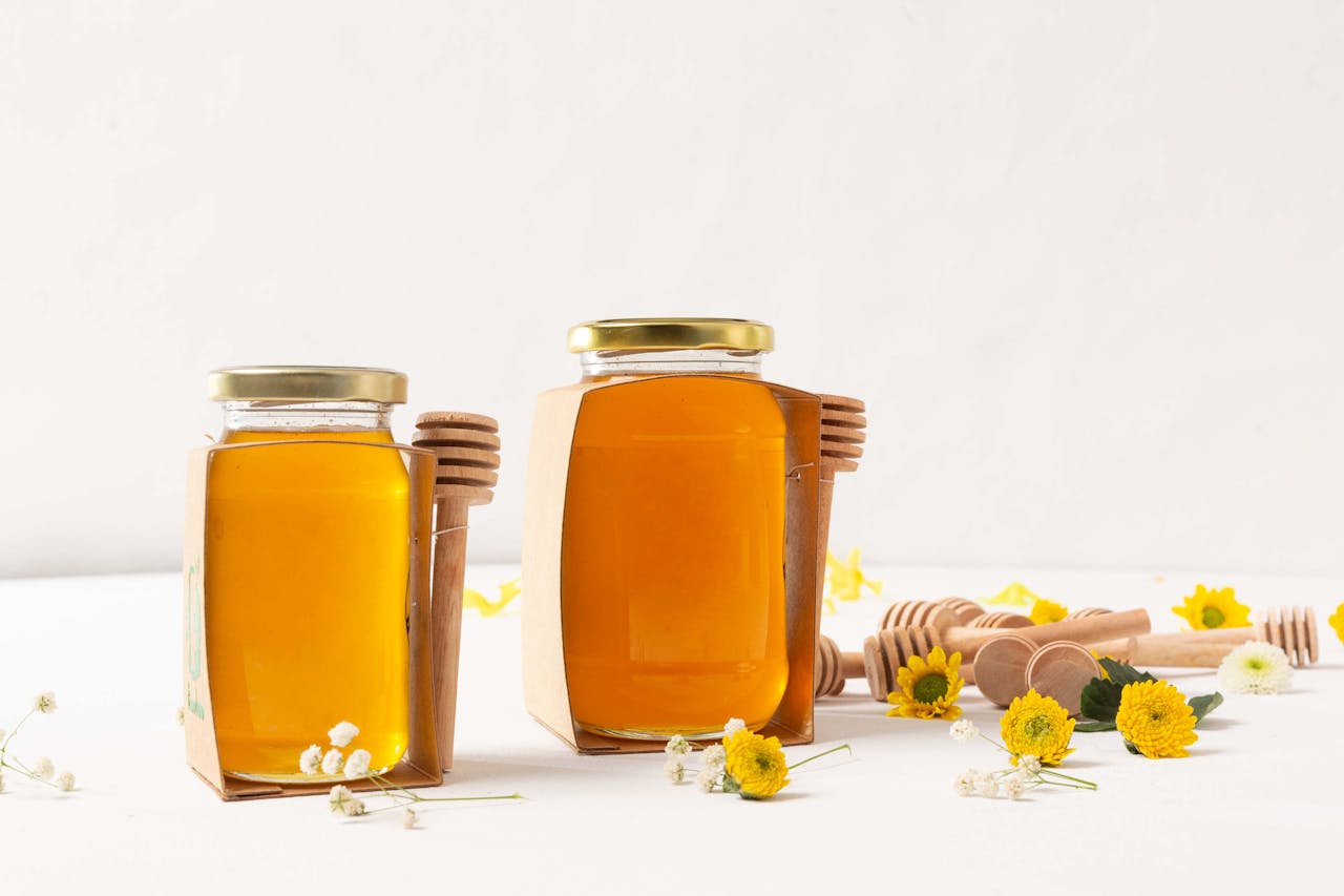 services-01 Aesthetic portrayal of honey jars with dippers and flowers on a white background.