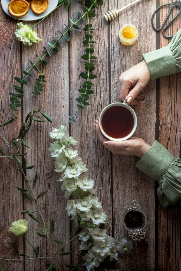 A cozy flat lay of a tea cup held over a wooden table with flowers and honey, evoking a rustic vibe.