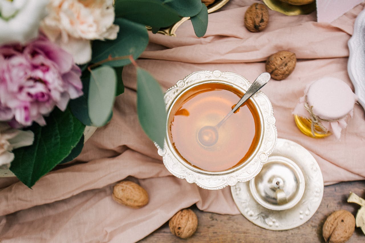 A luxurious silver bowl of honey surrounded by walnuts and floral decor on a pink cloth.